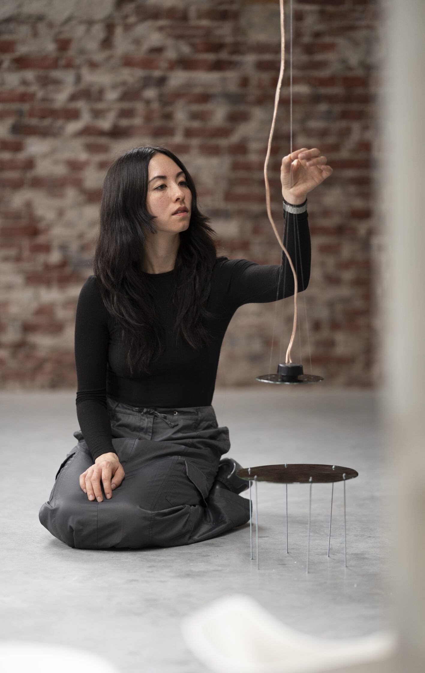 A person is kneeling in a gallery setting and holding their arm out to a wire suspended from the ceiling