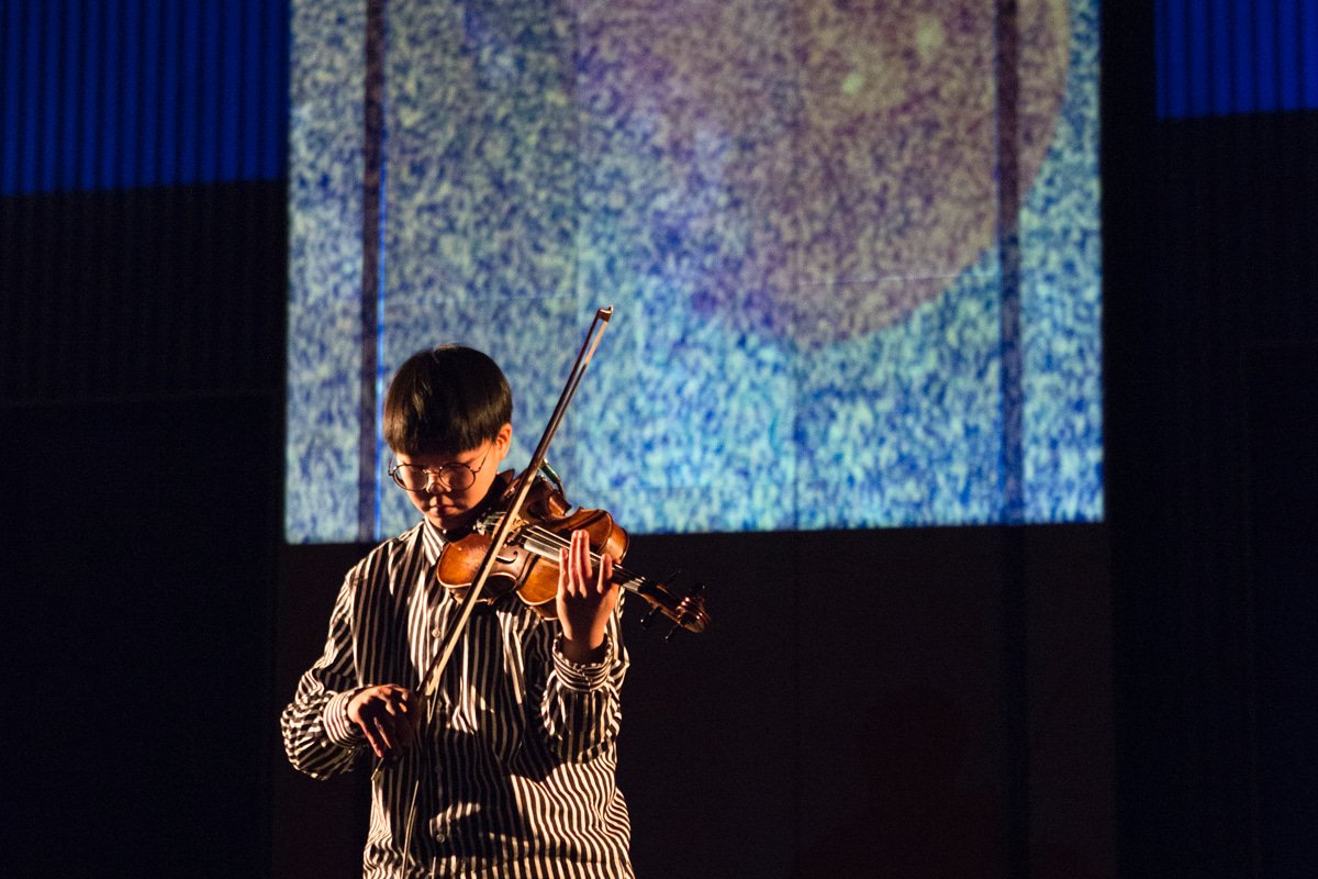 A violinist performs in front of projected images