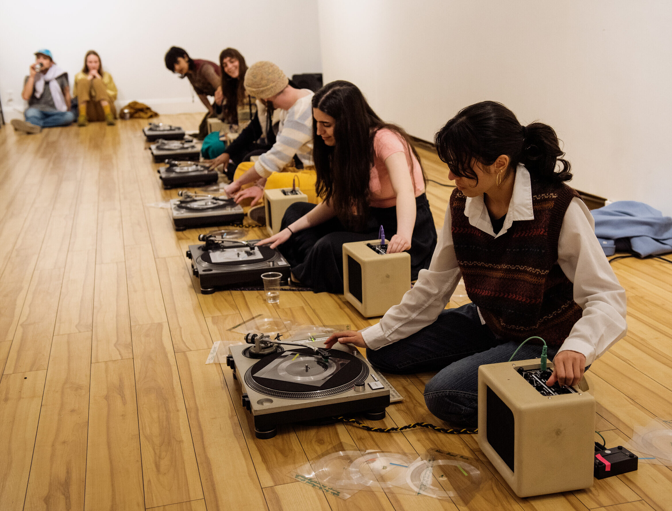 Six people are sitting on the ground manipulating direct-drive turntables